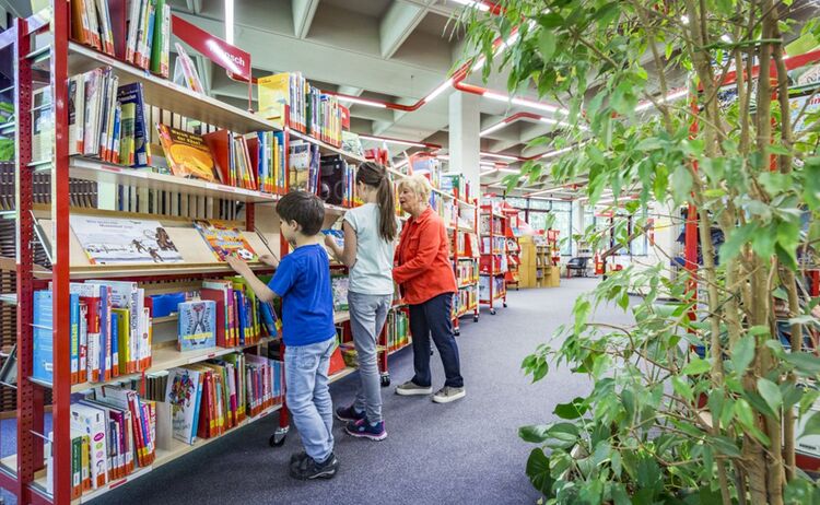 Familie beim Bücher aussuchen an den Regalen in der Kinderbuchabteilung: Zum Vergrößern auf Bild klicken