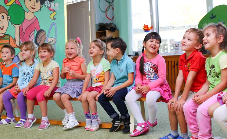 Kinder im Kindergarten, die auf einer Bank sitzen und lachen: Zum Vergrößern auf Bild klicken