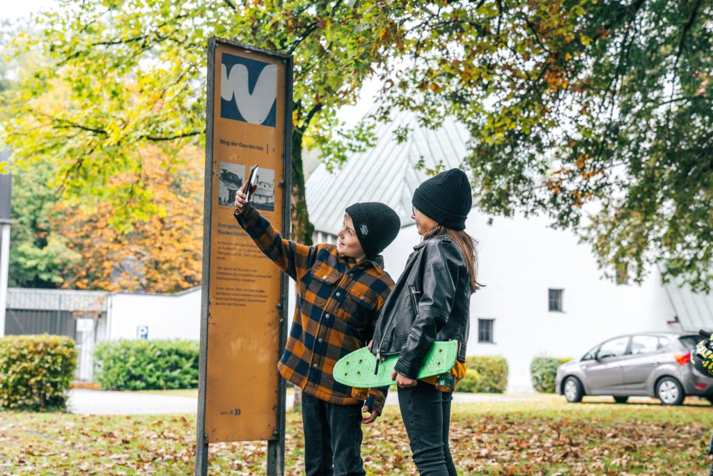 Ein Junge und ein Mädchen stehen vor einem Schild des Weg der Geschichte