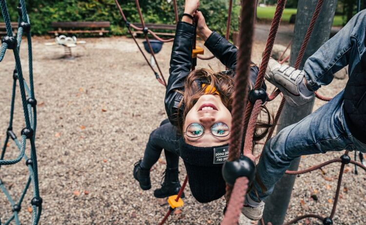 Ein Mädchen hängt kopfüber an einem Klettergerüst auf dem Spielplatz: Klick öffnet eine vergrößerte Ansicht