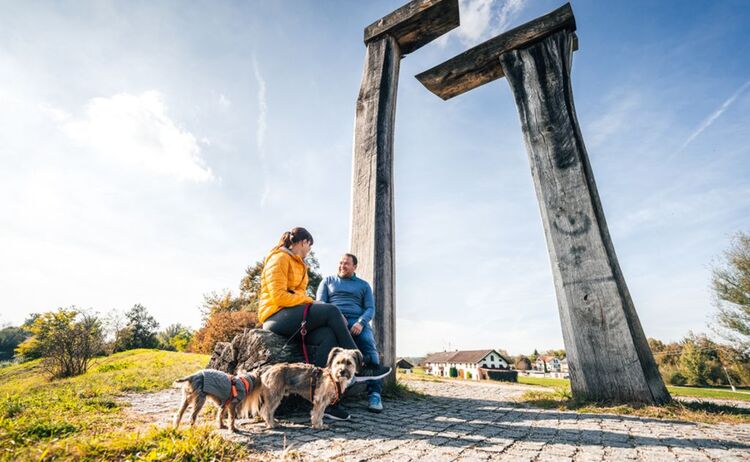 Eine Frau und ein Mann machen am Hochwasserdenkmal am Inn eine Pause mit ihren Hunden: Klick öffnet eine vergrößerte Ansicht