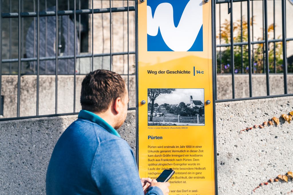 Ein junger Mann sieht sich ein Schild vom Weg der Geschichte an