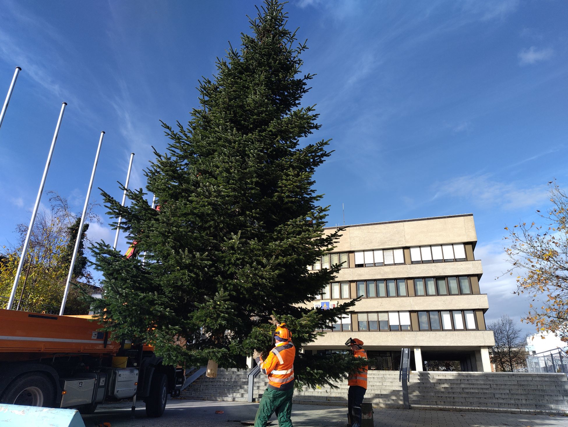 Zwei Mitarbeiter der Stadtwerke bauen den Christbaum vorm Rathaus mit einem Krank auf