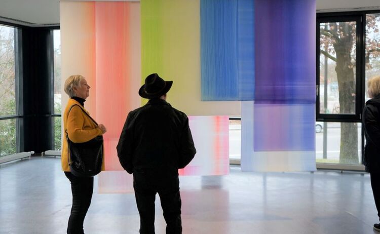 Gäste vor dem mehrteiligen Vorhang aus frei hängenden und farbig gestalteten Folien : Klick öffnet eine vergrößerte Ansicht