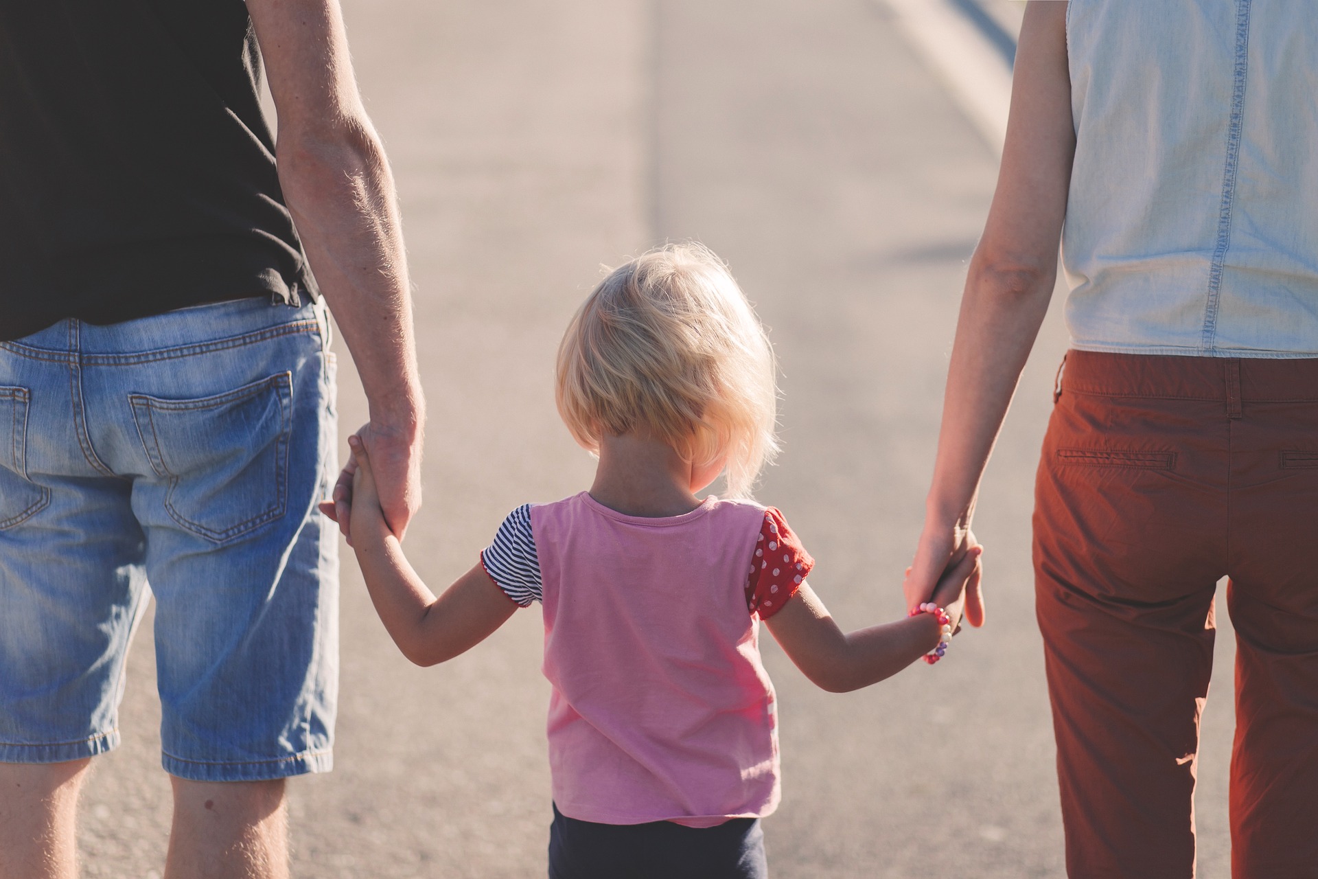 Symbolbild Vereinbarkeit Familie und Beruf, das ein kleines Kind mit seinen Eltern Hand in Hand zeigt