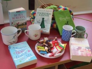Ein Tisch bestückt mit Büchern, Kaffeetassen, Stricksachen und einem Teller mit Schokolade