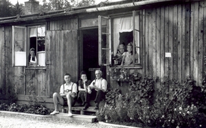 Im Fl&uuml;chtlingslager, 1948, drei Personen sitzen vor, weitere Personen schauen aus den Fenstern der Baracke.-foto