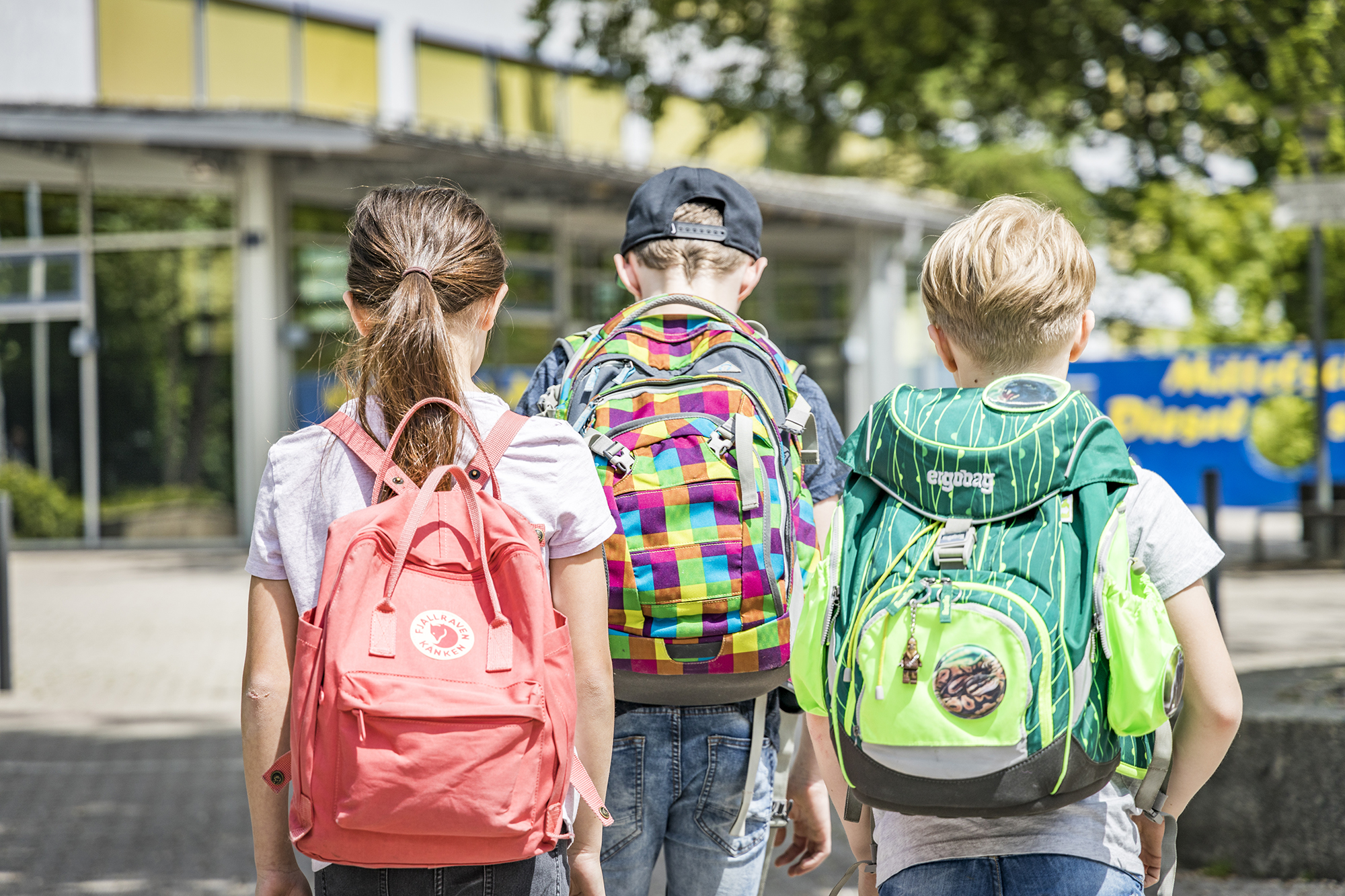 Schulkinder von hinten mit ihren Rucksäcken 