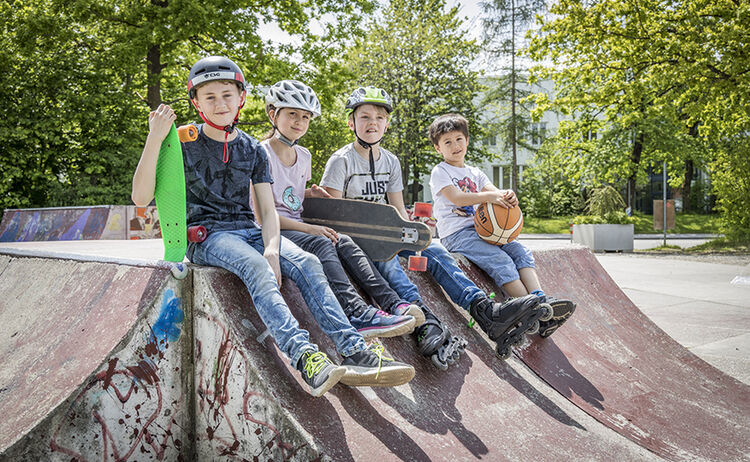 Vier Kinder sitzen auf mit ihren Skateboards auf einer Bahn im Skaterpark : Klick öffnet eine vergrößerte Ansicht