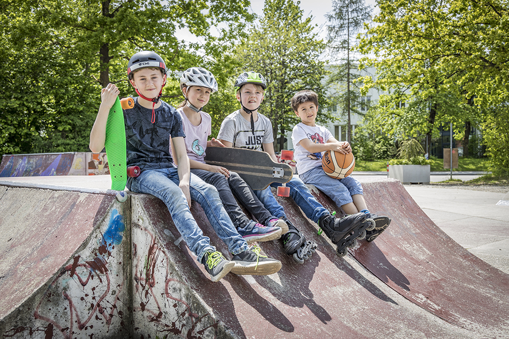 Vier Kinder sitzen auf mit ihren Skateboards auf einer Bahn im Skaterpark 