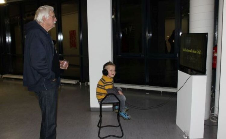 Ein Großvater sieht sich mit seinem Enkel einen Film in der Ausstellung modern vormodern an : Klick öffnet eine vergrößerte Ansicht