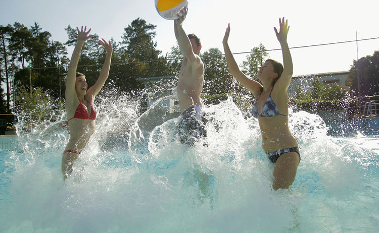 Zwei Frauen und ein Mann spielen Wasserball im Wellenbecken im Waldbad: Zum Vergrößern auf Bild klicken