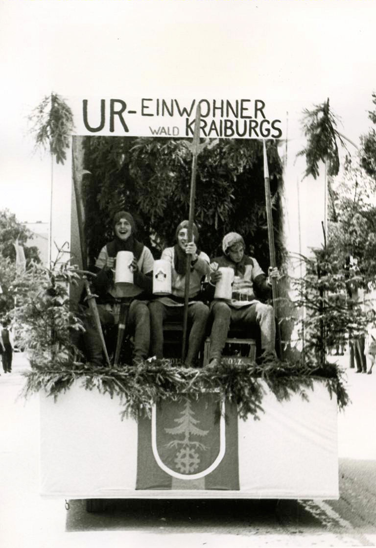 Faschingsumzug 1970 mit drei jungen Männern auf einem Umzugswagen zum Thema "Ur-Einwohner"