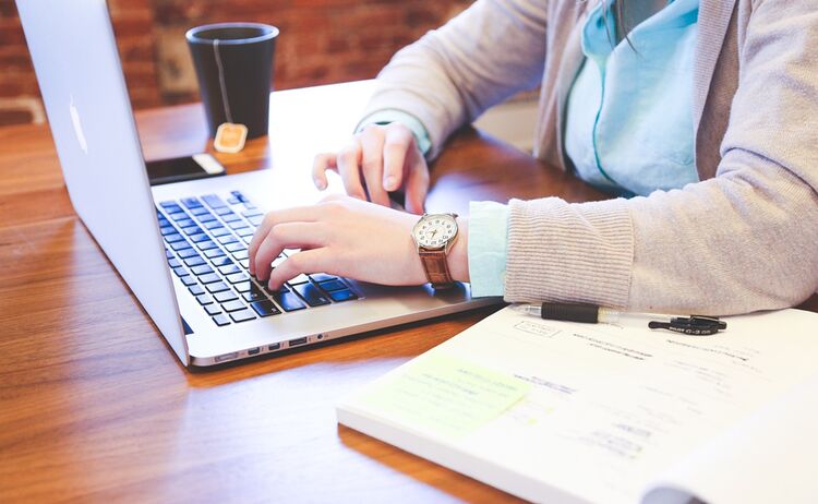 Sinnbild für Digitalisierung: Eine Person die an einem Schreibtisch am Laptop sitzt: Zum Vergrößern auf Bild klicken