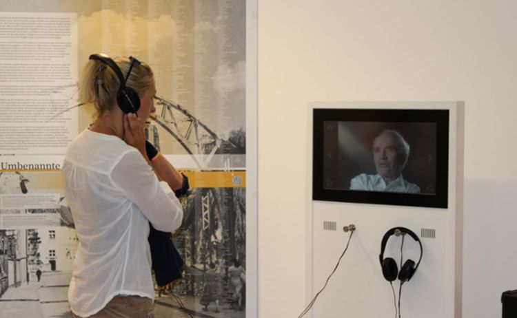 Eine Besucherin hört sich mit Kopfhörern ein Interview der Ausstellung Verschwundene Orte an: Zum Vergrößern auf Bild klicken